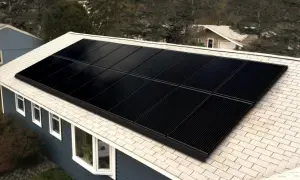 Paneles negros de una aplicacion placas solares cubren el tejado de una casa azul, rodeada de árboles.