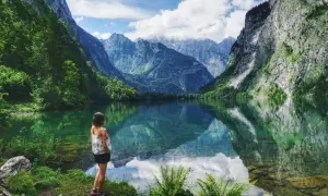 Frau blickt auf spiegelglatten See in den bayerischen Regionen, umgeben von steilen, bewaldeten Bergen.