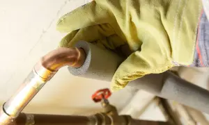 Mit gelben Handschuhen werden Heizungsrohre isoliert, um Energie zu sparen.