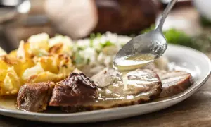 Łyżka polewa pieczoną karkówkę aromatycznym sosem. Obok ryż i złociste ziemniaki.