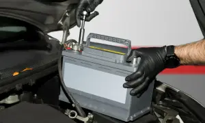Mechanik w czarnych rękawiczkach montuje akumulator samochodowy, przygotowując go do regeneracji.