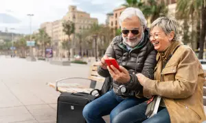 Uśmiechnięta para seniorów na ławce w mieście przegląda telefon. Czyżby sprawdzali, co to roaming, planując kolejną podróż?