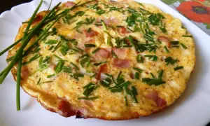 Puszysty omlet ze szczypiorkiem i kawałkami wędliny, podany na białym talerzu.