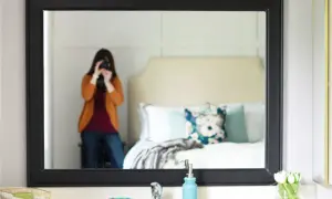 A person takes a selfie in a mirror with a black frame, showcasing a bedroom and a DIY mirror frame project.