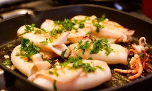 Seppie alla griglia succulente, cosparse di prezzemolo fresco, cuociono in una padella scura, pronte per essere gustate.