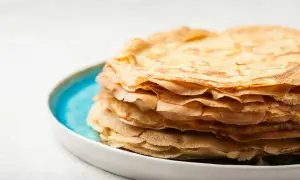 En hög med gyllene pannkakor, gjorda med vatten istället för mjölk, ligger på en blå och vit tallrik.