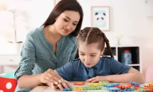 Terapeutka pomaga dziewczynce z upośledzeniem w stopniu umiarkowanym układać kolorowe puzzle.