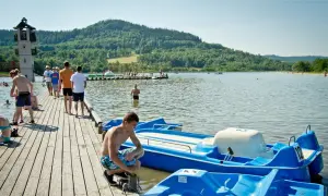 Letnie popołudnie nad jeziorem, gdzie można podziwiać śląskie atrakcje. Ludzie spacerują po molo, pływają i relaksują się przy wodzie.