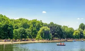 Słoneczny dzień w Hyde Park w Londynie. Ludzie odpoczywają nad jeziorem, niektórzy pływają łódkami.