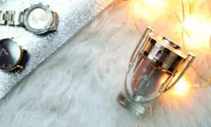 Flakon perfum Invictus Intense na białym futerku, obok błyszczącej powierzchni z zegarkami i ciepłe światła.