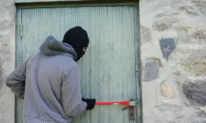 Un individu masqué tente de forcer une porte avec un pied-de-biche, acte relevant du cambriolage et du code pénal.