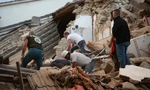 Ratownicy przeszukują gruzy po trzęsieniu ziemi we Włoszech. Ludzie w kaskach i kamizelkach pracują wśród zniszczonych budynków, szukając ocalałych.