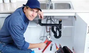 Hydraulik z kluczem w ręku, gotowy do pracy przy instalacji pod zlewem. Jego kod zawodu to hydraulik.