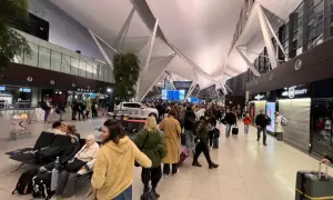 Tłum ludzi w terminalu lotnisko gdańsk odloty. Wszyscy czekają na swoje podróże, niektórzy siedzą, inni idą z bagażami.