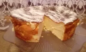 Puszysty sernik z mlekiem skondensowanym, oprószony cukrem pudrem, prezentuje się apetycznie na szklanej paterze.