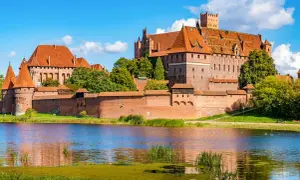 Die imposante Marienburg Burg, eine mittelalterliche Festung aus rotem Backstein, thront über einem ruhigen See.