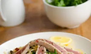 Un piatto di spaghetti con tonno fresco, rucola, capperi e una fetta di limone.
