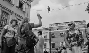 Uliczna fotografia: człowiek balansuje na linie, tłum obserwuje.