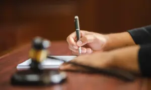 Dłoń referendarza sądowego pisze długopisem na papierze, obok leży młotek sędziowski.