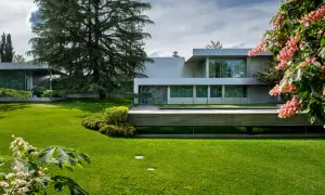 Casa moderna rodeada de jardines bonitos, césped verde y flores rosadas.