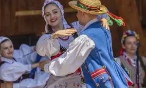 Para tańczy w tradycyjnych strojach ludowych, celebrując muzykę folkową.