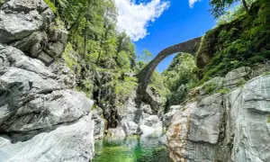 Idyllische Schlucht mit Steinbrücke, ideal für Tessin Wandern. Türkisgrünes Wasser fließt zwischen Felsen.