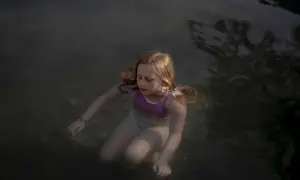 Bambina con capelli biondi immersa nell'acqua scura, un'immagine che evoca la serenità e la purezza, tipica delle opere di Laura Pannack.