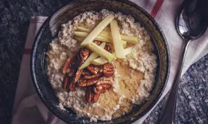 Porridge zubereiten: Cremiger Haferbrei mit Apfelspalten, Pekannüssen und Honig in einer Schüssel, daneben ein Löffel.