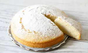 Una soffice torta all'acqua, cosparsa di zucchero a velo, con una fetta tagliata che ne mostra la morbidezza.