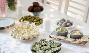 Stół zastawiony pysznymi przystawkami na imprezę domową: roladki z tortilli, szpinakowe roladki z łososiem, mini caprese, kulki czekoladowe i dipy.