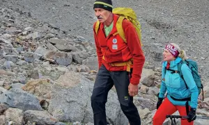 Simon Gietl und eine Frau wandern auf einem felsigen Berghang. Sie tragen Rucksäcke und Wanderkleidung.