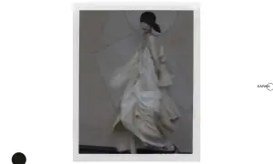 Modelka w zwiewnej, kremowej sukni i czarnym kapeluszu, w stylu Sarah Moon, porusza się z gracją.