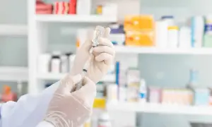 Ręce w rękawiczkach przygotowują zastrzyk. W tle apteczne półki z lekami, sugerujące przygotowania do szczepień na przykład na Madagaskarze.