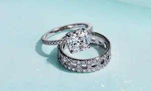 Un anillo de compromiso con un gran diamante cuadrado reposa sobre un anillo de matrimonio con incrustaciones de diamantes, ambos de plata.
