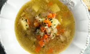 Zupa warzywna w białej misce z ziemniakami, marchewką i szczypiorkiem.
