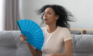 Kvinna med lockigt hår fläktar sig intensivt, uppenbart besvärad av värmen. Kanske upplever hon **svettningar gravid** och söker lindring.