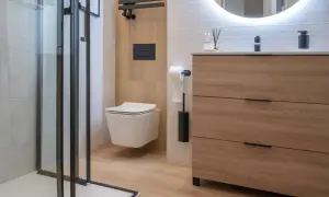 Modernos baños blancos y madera clara, con ducha de cristal, inodoro suspendido y mueble de cajones.