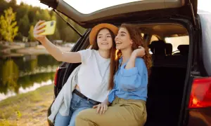 Dwie przyjaciółki robią sobie selfie przy samochodzie nad jeziorem. Idealny weekend z przyjaciółką!