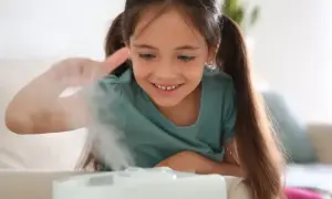 Uśmiechnięta dziewczynka bawi się mgiełką z nawilżacza powietrza dla niemowląt, tworząc magiczną atmosferę w pokoju.