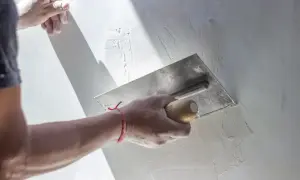 Ręka z kielnią wygładza świeżą masę podczas gipsowania ścian.