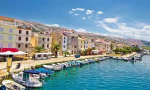 En kuststad i Kroatien med färgglada hus, en hamn full av båtar och en bergig bakgrund. Här finns fakta om Kroatien.