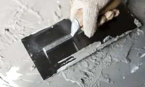Ręka w rękawicy rozprowadza gips szpachlowy lub budowlany kielnią po powierzchni.