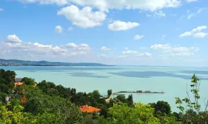 Widok na turkusowe wody Balatonu z zielonymi wzgórzami i domami. To jedno z najpiękniejszych miejsc nad Balatonem, z molo i żaglówkami na horyzoncie.