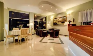 Eleganckie wnętrze recepcji Villa Plaza Warszawa. Wygodne fotele, stolik z kwiatami i luksusowy lada.