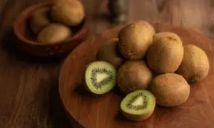Kiwi, noti per essere tra i cibi che fanno andare in bagno, sono disposti su un tagliere di legno. Uno è tagliato a metà, mostrando la polpa verde e i semi neri.