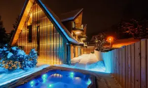 Nowoczesny dom w Zakrzewie oświetlony ciepłym światłem, z podświetlanym jacuzzi w śnieżnej scenerii.