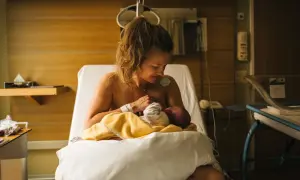 Nybliven mamma ammar sitt barn på en sjukhussäng. En lugn stund efter förlossningen, kanske inför en efterkontroll på MVC.