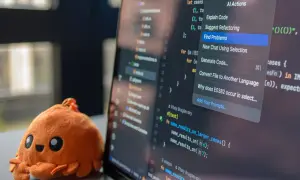 Un adorable crabe en peluche à côté d'un écran d'ordinateur affichant du code. Le menu contextuel propose des actions IA, aidant à choisir quel langage de programmation apprendre.