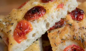 Nahaufnahme von Focaccia, einem der beliebtesten italienischen Brotsorten, mit getrockneten Tomaten und Kräutern bestreut.