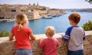 Drei Kinder blicken auf die Bucht von Valletta, Malta. Ein kleiner Junge, der fast wie ein Baby wirkt, steht in der Mitte.